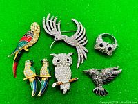 Full view of all 6 pieces including 5 bird brooches and 1 owl ring on green background