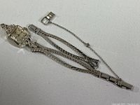 Entire watch laid flat showing case, braided band and safety chain