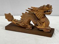 Side view of ornately carved wood dragon figure showing layered wood detailing and rectangular base.