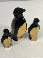 Three brass penguin figurines with black painted coats, shown in a group on a white surface