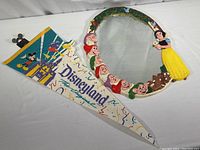 Top view of Disneyland felt pennant next to Snow White and Seven Dwarfs oval mirror on white surface.
