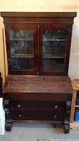 Front view of antique wooden desk with closed glass paneled hutch doors and closed drop front writing surface.