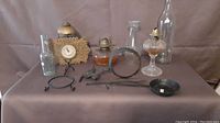 Wide view of entire lot showing clock, lamp parts, bottles, and iron tools on table