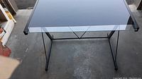 Oblique view of the desk showing the black metal frame and glass top, highlighting the support structure.