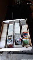 Box of assorted sports cards with hockey and basketball cards mostly visible