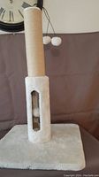 Photo of new cat scratcher toy with plush base and sisal-wrapped post with two pom-pom toys hanging