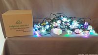 Two sets of JuSsit G40 copper wire string lights arranged with an extra replacement bulb and the product box labeled 'JuSsit Enlighten your life! G40 Copper Wire String Lights COLOR: RGB MADE IN CHINA'. Multi-color RGB lights appear to be on.