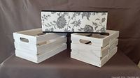 Three white wooden baskets shown on brown background; two plain wooden slatted crates and one fabric-lined box with floral pattern.