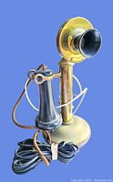 Front view of the brass candlestick phone with black earpiece and fabric-covered cord coiled beside it.