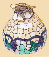 Photo of stained and leaded glass hanging light shade with grape cluster and leaf motifs, cream-colored glass panels, and hanging chain.