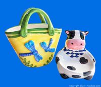 Front view of yellow ceramic basket with green handles and two blue butterflies, plus cow-shaped ceramic figurine with black spots and pink snout