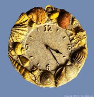 Front view of the sea shell analog wall clock showing detailed shell decoration around the face with hour numbers 12, 3, 6, and 9 and black clock hands.