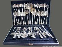 Silverware set displayed inside black case with spoons and serving utensils on upper portion and forks and knives on bottom.
