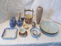 Collection of ten assorted Chinese porcelain and stoneware items arranged on a white cloth background. Includes two fish-shaped teapots, a duck-shaped teapot, two 9-inch stoneware bowls with floral branch design, a 4-inch bud vase, a well planter with basket handle, finger bowls with underplate, and small dishes.