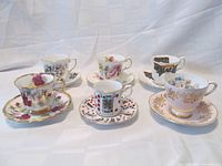 Photo of 6 fine bone china teacup and saucer sets arranged on white cloth background. Five teacups with matching saucers and one demi-tasse set displayed to show patterns and details.