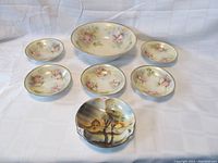 Photo showing large serving bowl, five smaller dessert bowls with pink and white roses, and one bowl with a colorful landscape scene.