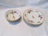Stack of 4 fruit/dessert bowls on the left and 4 salad plates on the right showing floral design and gold trim.