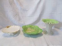 Set of three Royal Winton porcelain decorative items: green Lustreware vase with flower-shaped top and center stem, green Relief Ware embossed vegetable serving dish, and white Petunia White compote with gold floral accents.