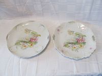Two decorative porcelain plates side by side, showing floral designs and handles