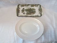 Both porcelain serving dishes displayed on white background, rectangular scenic dish on top and oval floral platter below