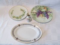 Four porcelain items: two plates, one serving platter, and one bud vase arranged on white background.