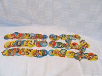 Wide view of 144 colorful circular candy lids arranged in rows on a white surface, showing varied cartoon designs and colors.