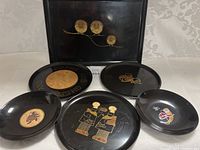 Display of six decorative black metal plates with vintage chef and food imagery, accompanied by a rectangular serving tray with gold flower motifs.