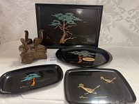 Photo showing all four items: three black lacquer trays with Couroc art and one wooden bird sculpture.