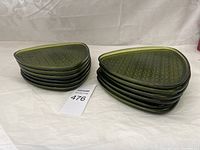 Two stacks of six green glass plates each, totaling twelve plates, arranged on a white surface. Plates have a subtle texture showing floral patterning and a triangular shape with rounded corners.