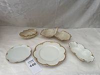Overview of five white porcelain serving pieces with gold scalloped edges, including plates and bowls