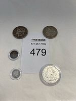 Five collectible coins arranged with lot number card: two Morgan silver dollars dated 1900 and 1896, Indian Head penny, and silver dime.