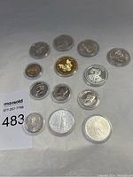 Photo showing 13 collectible coins in protective plastic cases with metallic silver and two gold-tone coins including JFK half dollars and others.