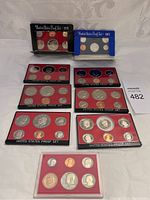 Overview of 9 United States Proof Sets arranged on a surface, showing packaging and multiple coins in each set.