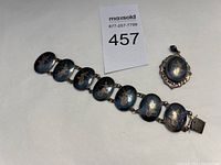 Photo showing the vintage Siam sterling silver bracelet alongside oval locket pendant with dark blue enamel and gold floral designs