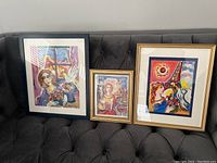 Three framed colorful prints by Zamy Steynovitz placed on a dark couch showing varied compositions and vibrant colors