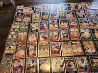 Top-down view of 110 baseball cards laid out on a wood surface in organized rows, displaying a variety of baseball legends from different teams and eras.