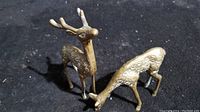 Two brass deer figurines on black surface, one standing upright and the other grazing.