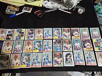 Full layout of 34 Steve Carlton baseball cards on a black surface with visible scissors, tape and pen in background
