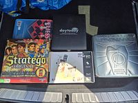 Five boxed games shown together in trunk. Silver Monopoly tin, Stratego Original box, Robots Play 601, black Daytoday folio for Albert Einstein games, and Classic Games Chess box.