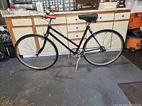 Full side view of black vintage bicycle showing frame, wheels, saddle, and handlebars with bell and red grips.