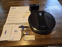 Robot vacuum with charging dock, two side brushes, HEPA filter, quick start guide and warranty card arranged on wooden table.