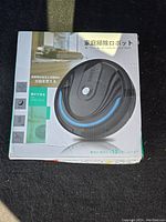 Front view of boxed electric robotic floor cleaner with black and blue design and Japanese text on packaging.