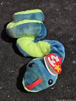 Blue and green plush snake with Ty tag visible, curved body seen from side.