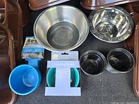 Various pet food bowls including large stainless steel bowls, plastic bowls, and packaged turquoise feeding bowls.