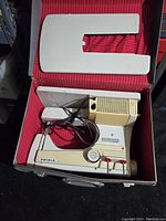 Portable sewing machine packed inside a red-lined carrying case with matching detachable plastic cover on top.