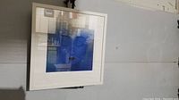 Framed blue face artwork titled 'Relaxation in Blue' hung on a grey wall, showing full view of the piece.