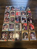 Top-down photo of 27 basketball trading cards featuring multiple NBA superstars arranged on wooden surface.