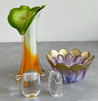 Front view of the green and orange vase, purple and gold bowl, and two small clear crystal bird figurines.