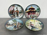 Four Asian style porcelain collector plates displayed with different traditional artwork and decorative borders