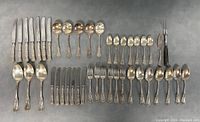 All silver plated flatware pieces laid out including 7 dinner knives, multiple spoons, forks, and serving utensils showing ornate handle details and tarnish.